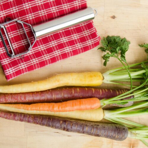 variety of carrots and a peeler lying on a cloth