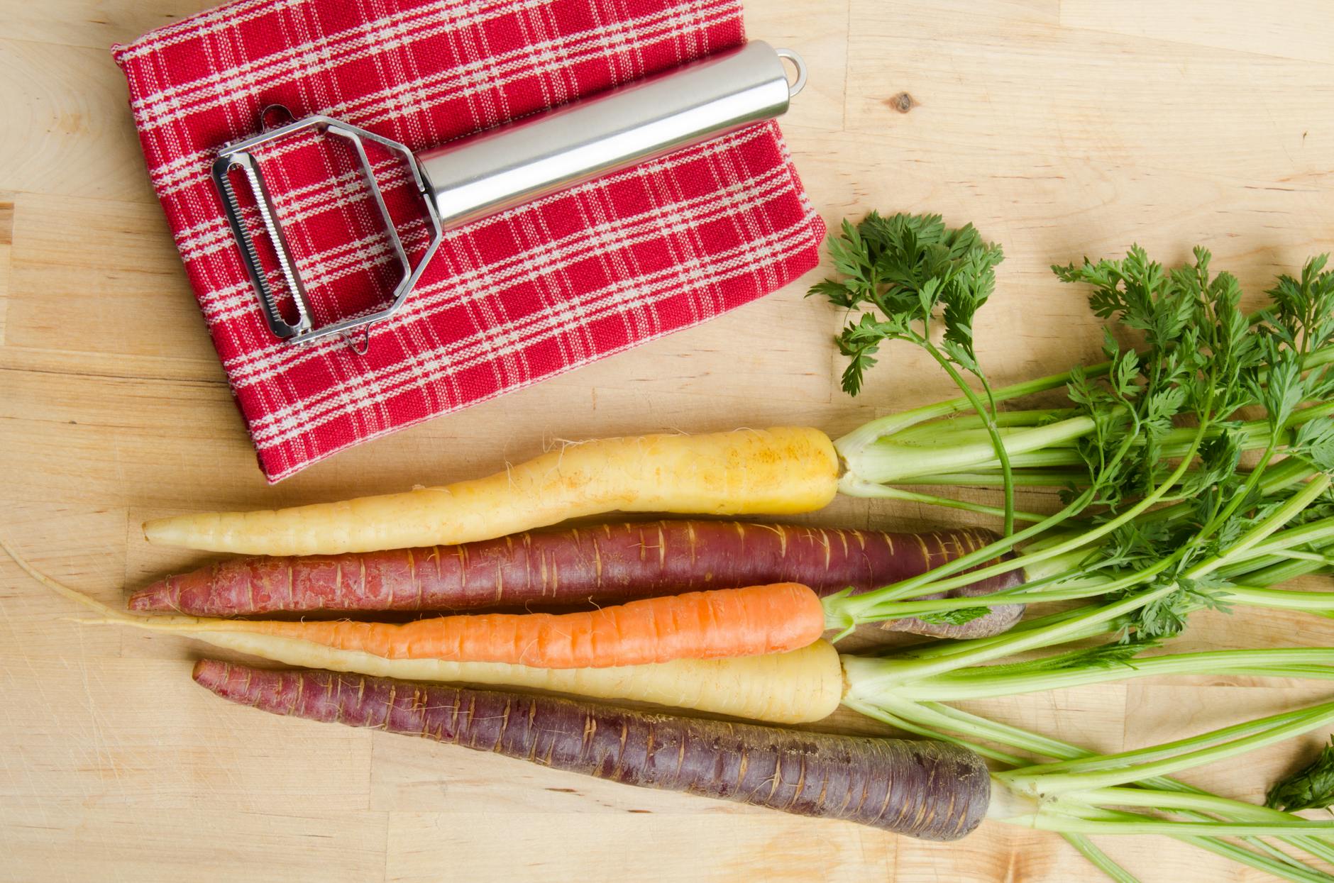 variety of carrots and a peeler lying on a cloth