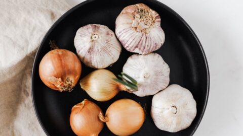whole onions and garlic bulbs on black dish