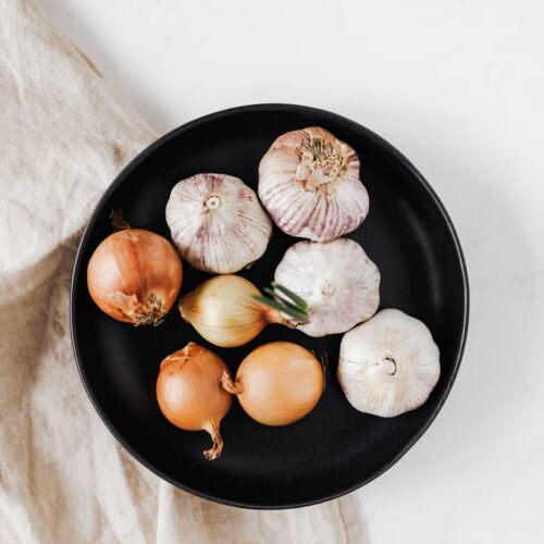 whole onions and garlic bulbs on black dish
