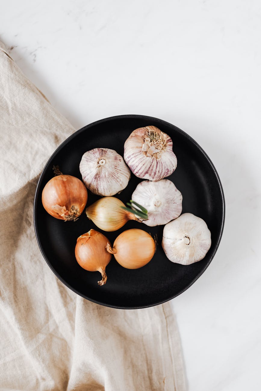 whole onions and garlic bulbs on black dish