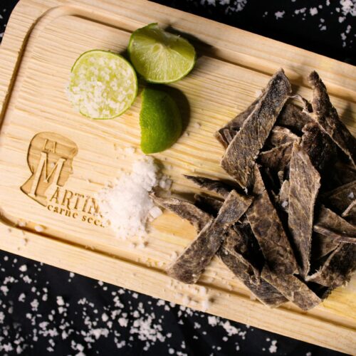 slices of meat o a wooden chopping board with lime and salt